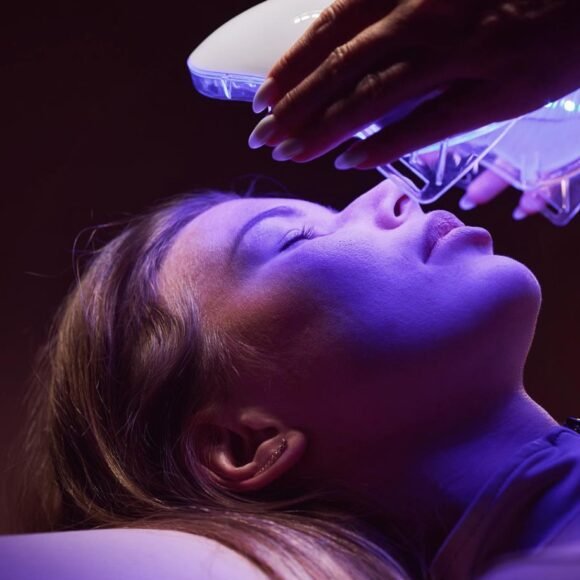 A person is receiving a facial treatment under a blue light therapy device.