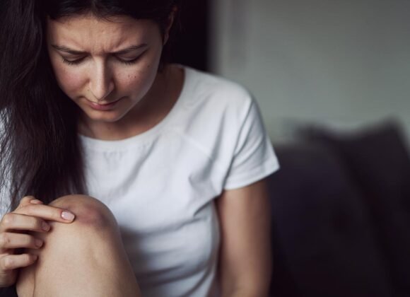 How to Stop Nighttime Itching from Eczema Symptoms A woman with long dark hair wearing a white shirt looks at a bruise on her knee.